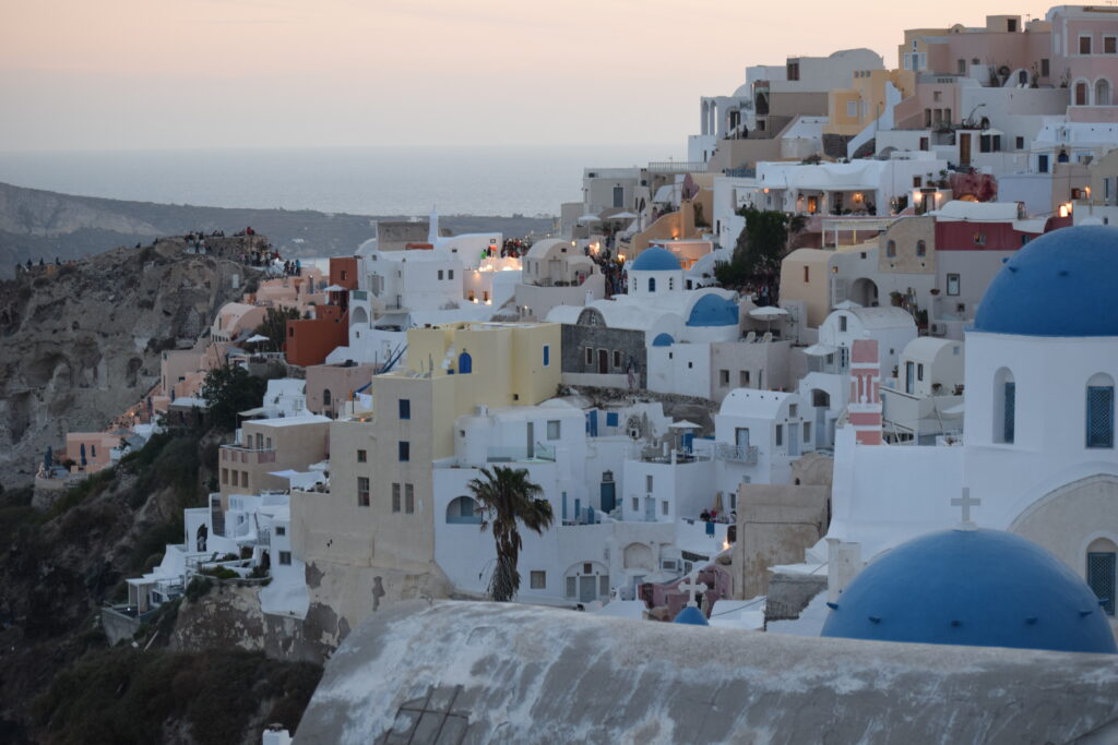 Looking over the side of Fira, Santorini Greece, with cave houses and churches with white walls and blue dome tops.