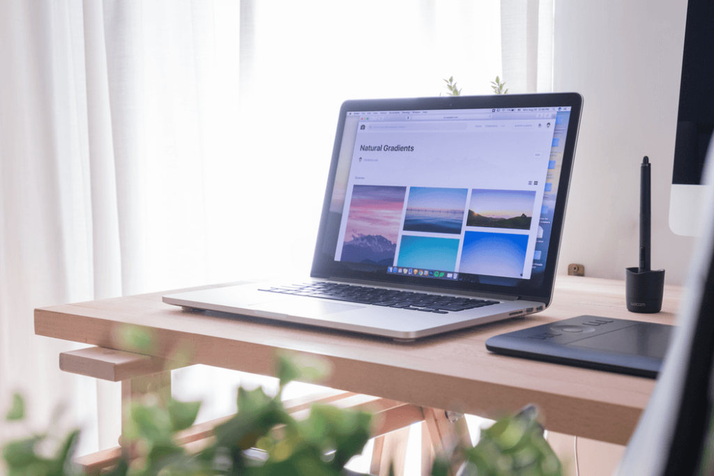 Open laptop on a wooden desk, with photos of different landscapes on the screen.