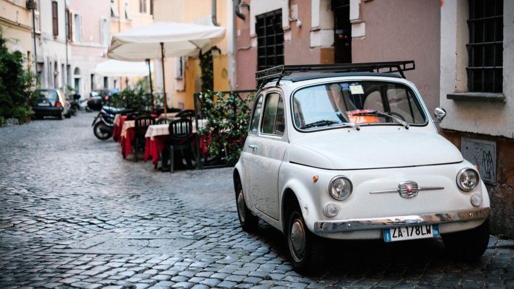 Small white car, parked in an alley on a cobblestone street.