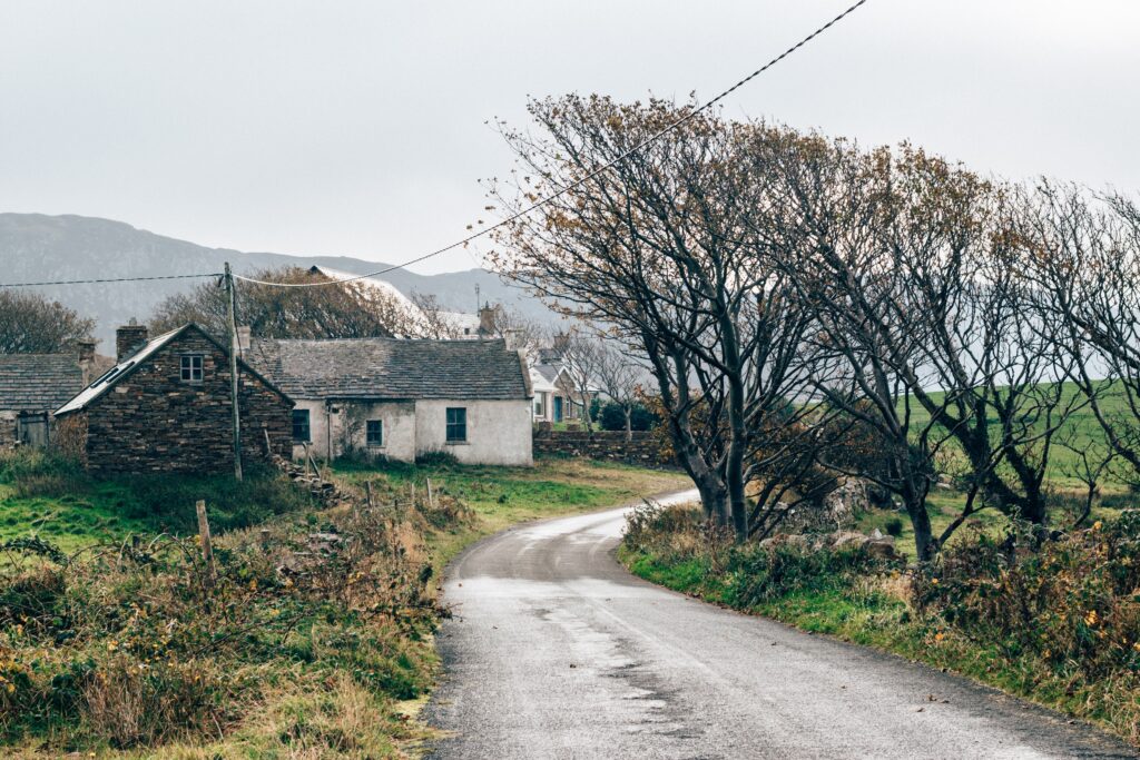 narrow, winding country road passing by an old stone home along the Ireland countryside.