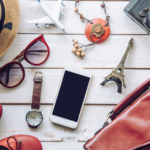 15 Amazing Travel Essentials For Your Next Getaway: sunglasses, watch, phone, hat,necklace, toy plane and eiffel tower
