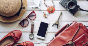 15 Amazing Travel Essentials For Your Next Getaway: sunglasses, watch, phone, hat,necklace, toy plane and eiffel tower